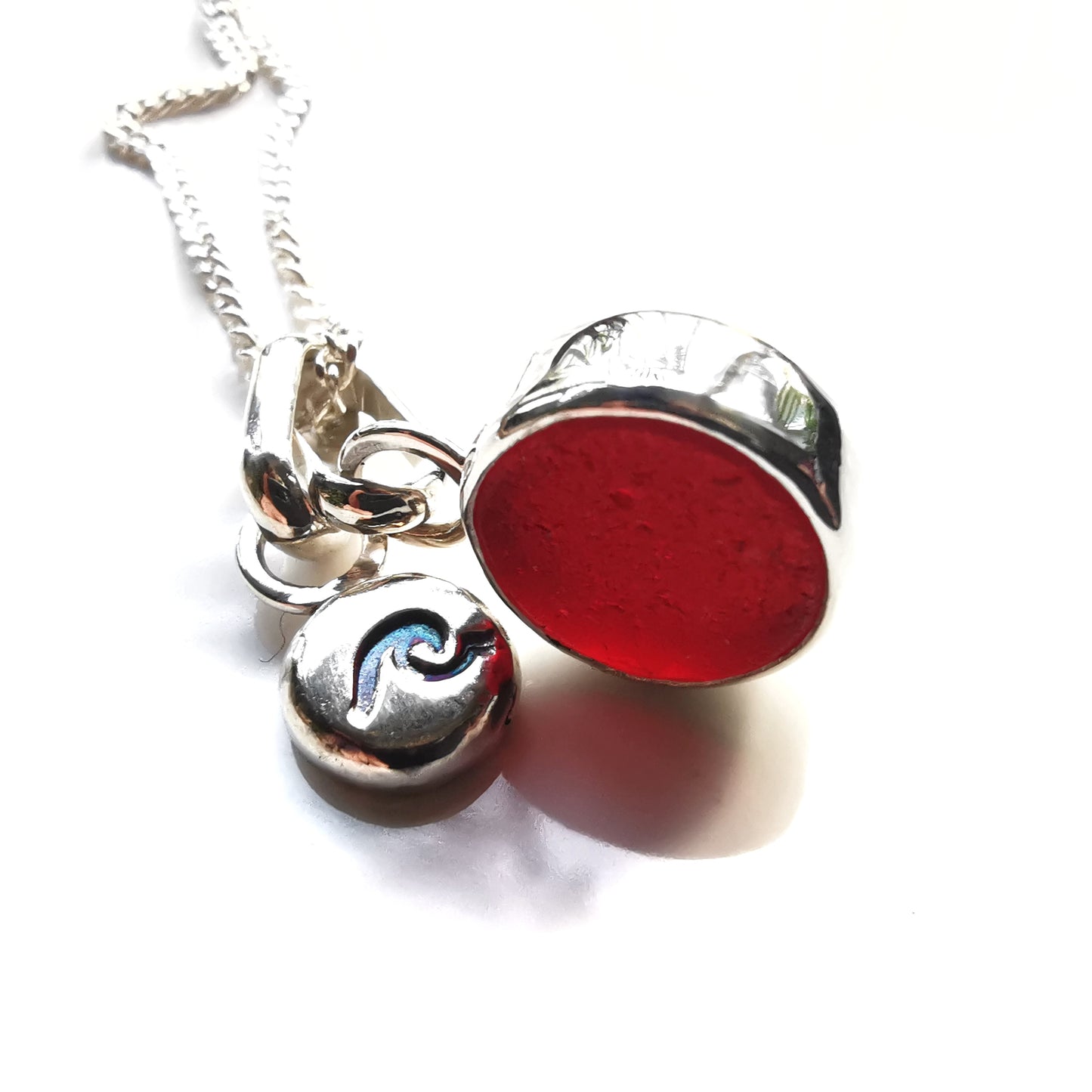 Scottish burgundy red sea glass and wave pebble duo of sterling silver pendants.