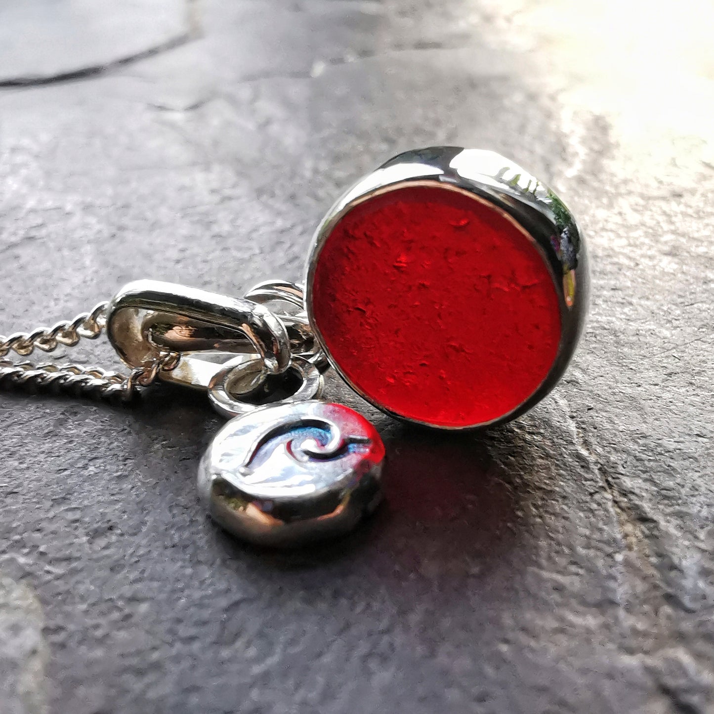 Scottish burgundy red sea glass and wave pebble duo of sterling silver pendants.