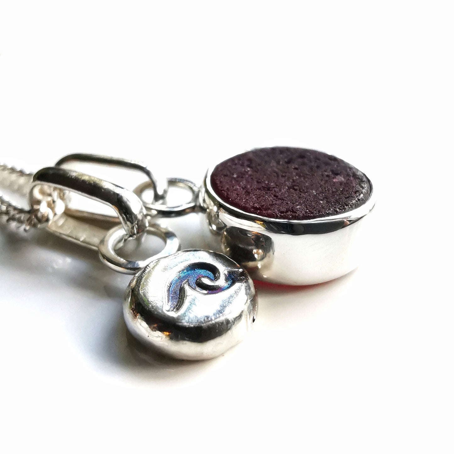 Scottish burgundy red sea glass and wave pebble duo of sterling silver pendants.