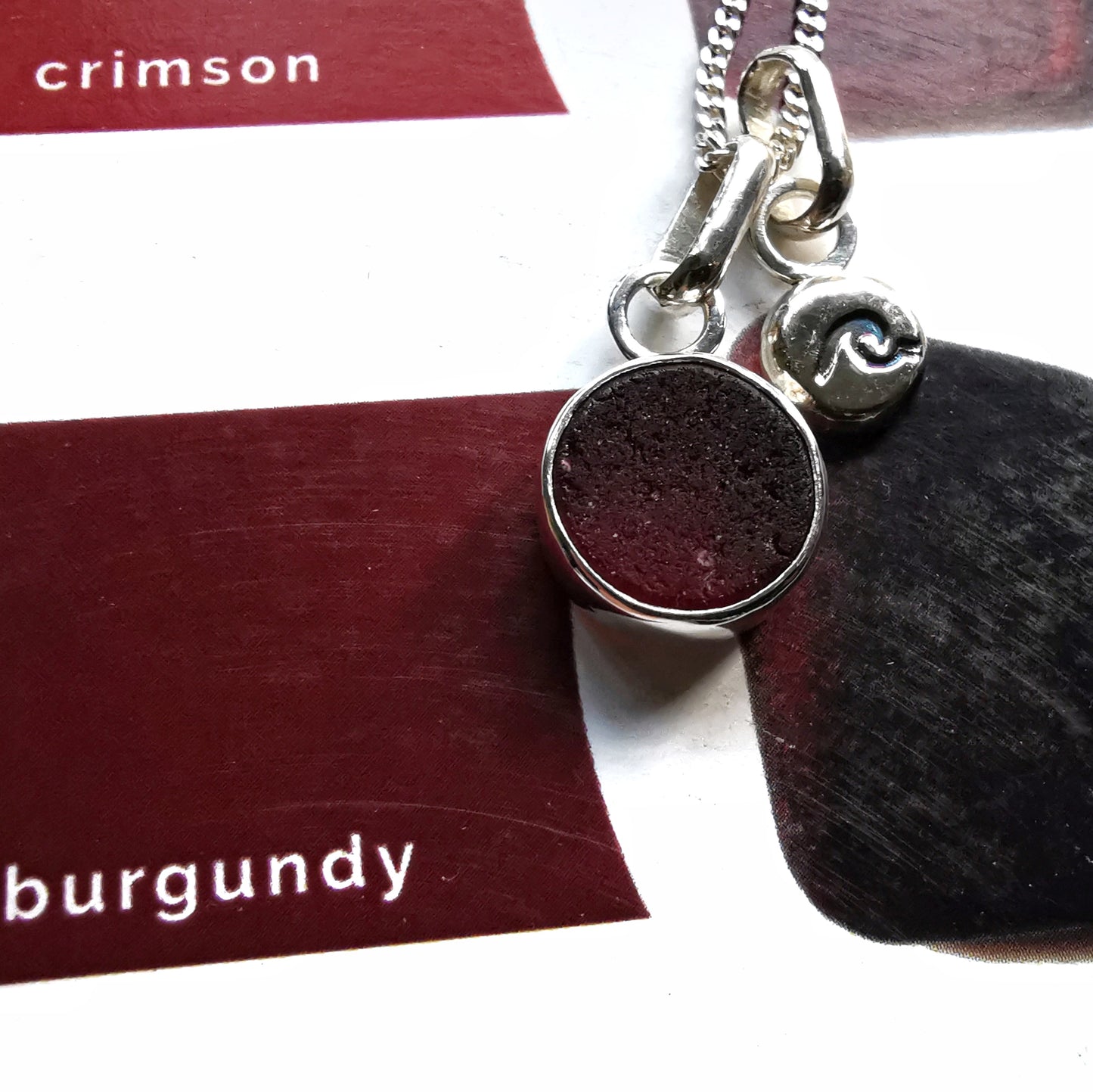 Scottish burgundy red sea glass and wave pebble duo of sterling silver pendants.
